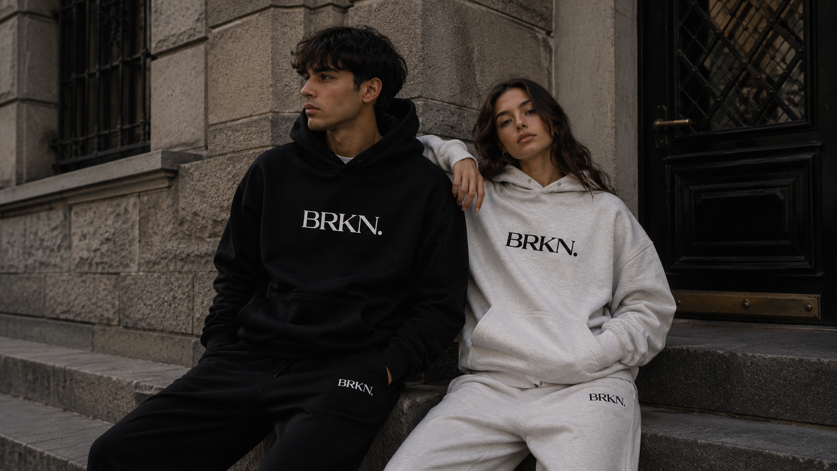 Man and woman in matching BRKN hoodies and sweatpants, urban streetwear style